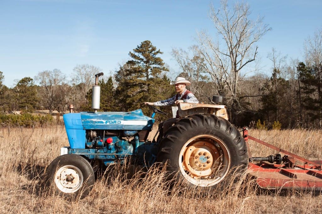 Landscaper driving a tractor with brush cutter through a field of tall grass